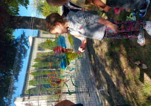 Dzieci malują farbami na folii rozwieszonej pomiędzy drzewami swoje wakacyjne wspomnienia